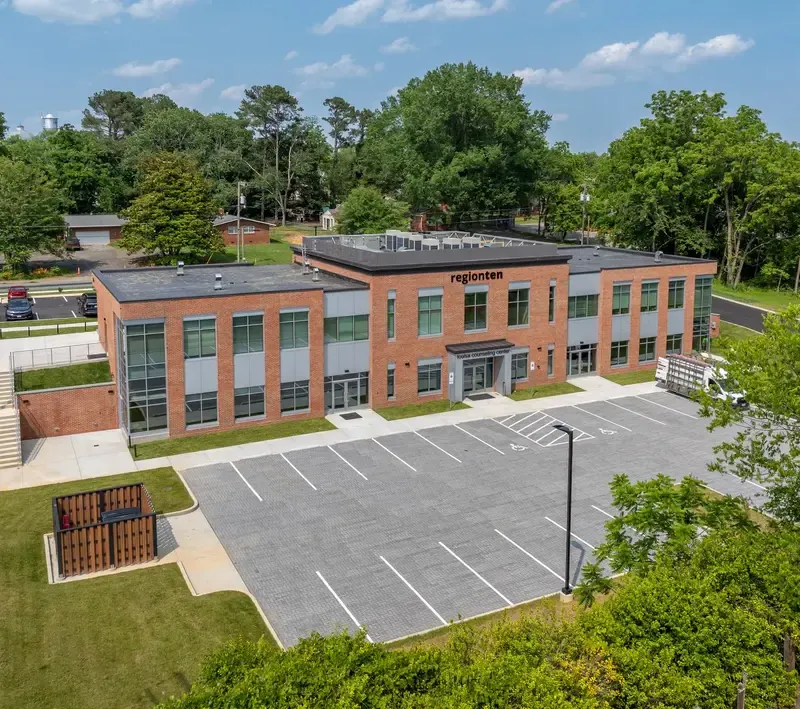 Aerial view of a two-story brick building surrounded by greenery, with an empty parking lot in front.